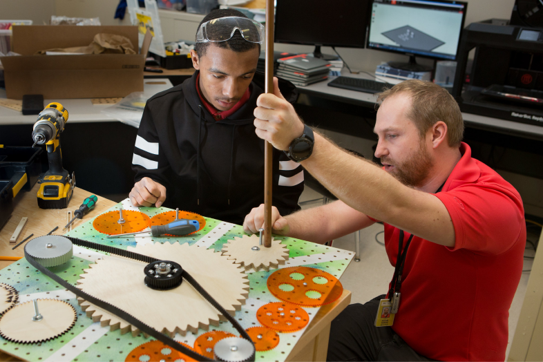 Male teacher helps male student with engineering project.