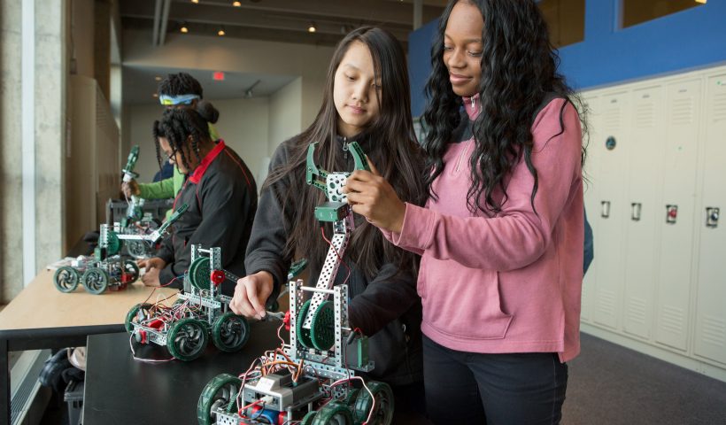 Two teenagers assemble a robot at their school.