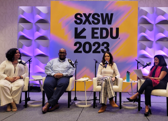 Four panelists sit in chairs on stage during a session at SXSW EDU 2023, where branded signage on the wall behind them is displayed.