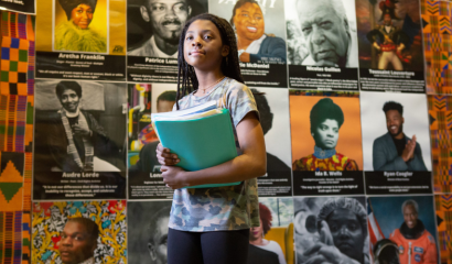 A Black girl stands in front of a Black History month display at Sutton Middle School in Atlanta. The display features iconic Black leaders, from Ida B. Wells to Aretha Franklin and Ryan Coogler.