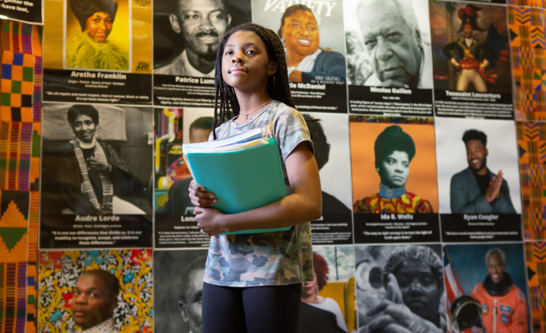 A Black girl stands in front of a Black History month display at Sutton Middle School in Atlanta. The display features iconic Black leaders, from Ida B. Wells to Aretha Franklin and Ryan Coogler.