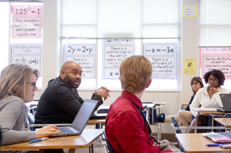 Teachers sit at desks in a classroom.