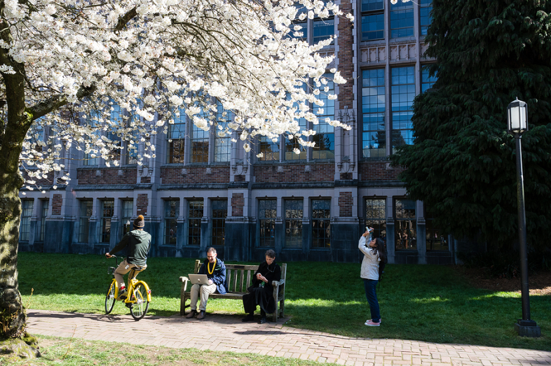 People sit, watch and ride bikes along a college campus.