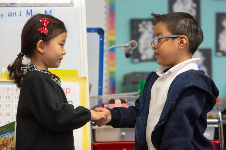 A kindergarten age girl and boy shake hands.
