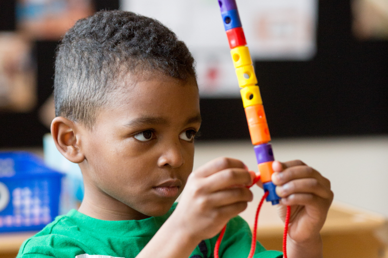 A preschool-age Black boy holds and stares at a Lego stick intently.