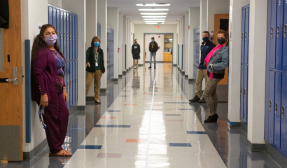 Teachers and students wearing face masks stand in a school hallway.