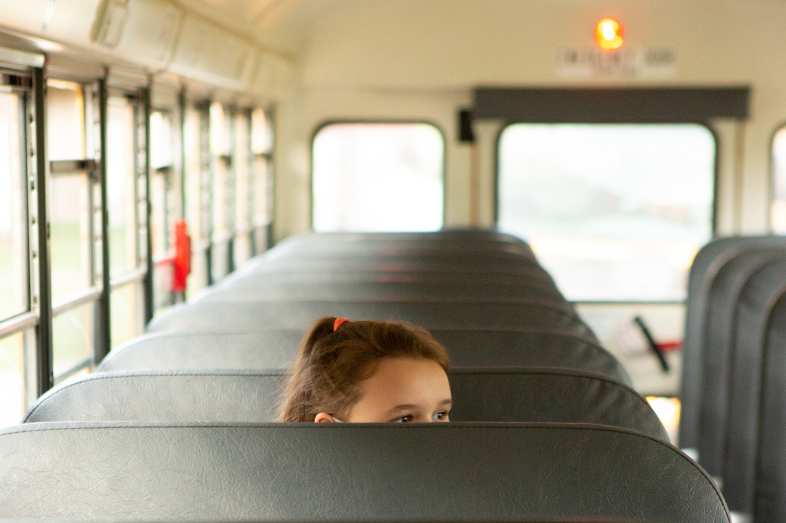 A elementary-aged girl sits alone on an empty school bus.