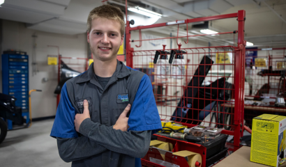 A young man stands in an auto shop, surrounded by machines and tools.