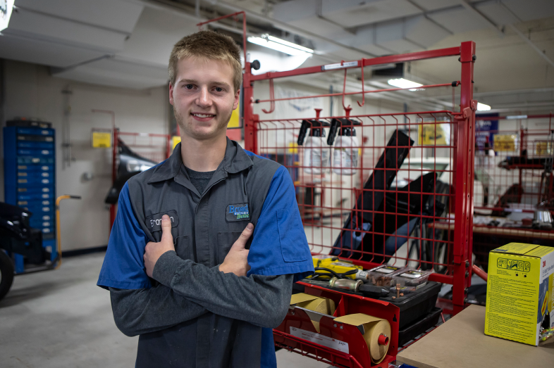 A young man stands in an auto shop, surrounded by machines and tools.