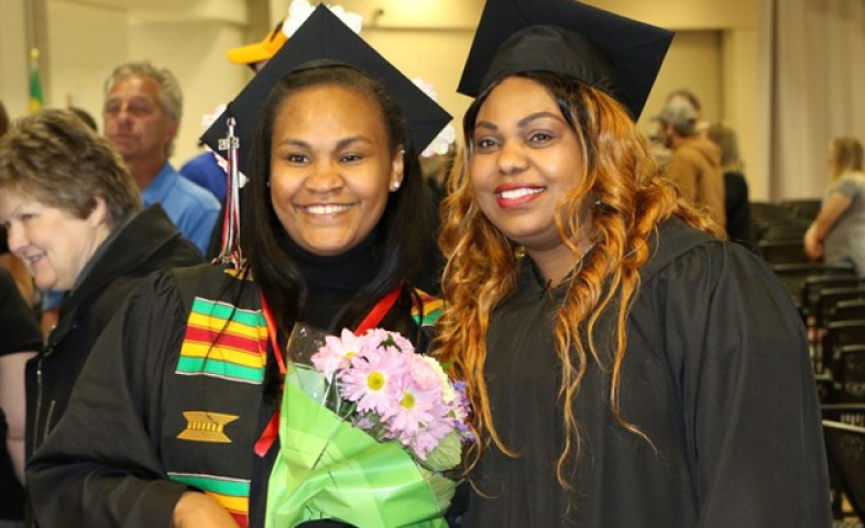 Two Black female college graduates pose side by side and smile for a photo.