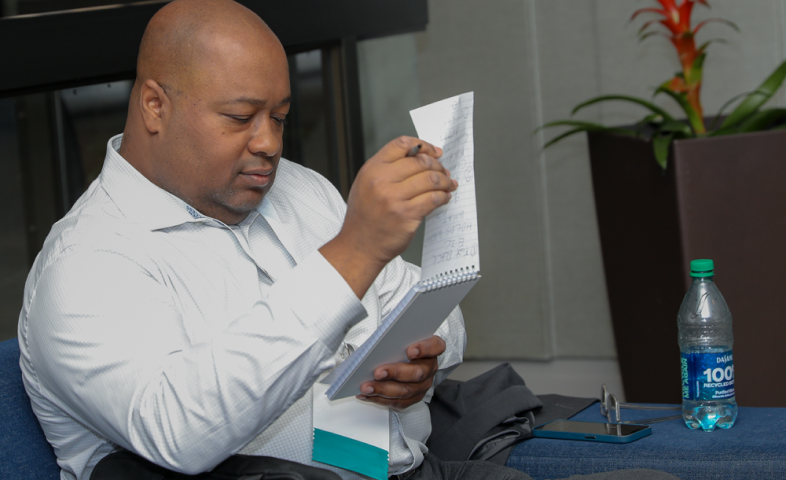 Wayne Carter, a journalist, looks through a reporting notebook while sitting.