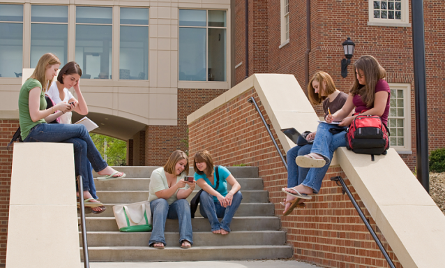 A group of college girls sit on the steps of a campus building.
