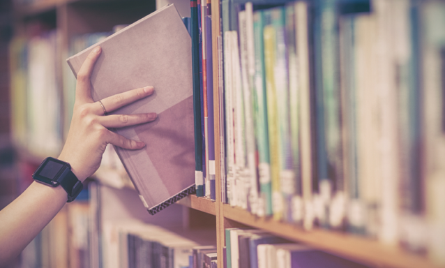 A hand is shown reaching for a book on a bookshelf.