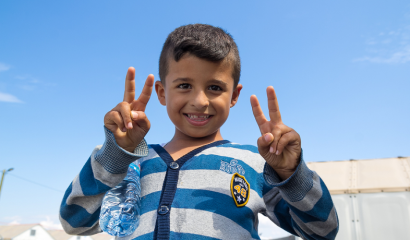 A little boy holds up four fingers and smiles at the camera.