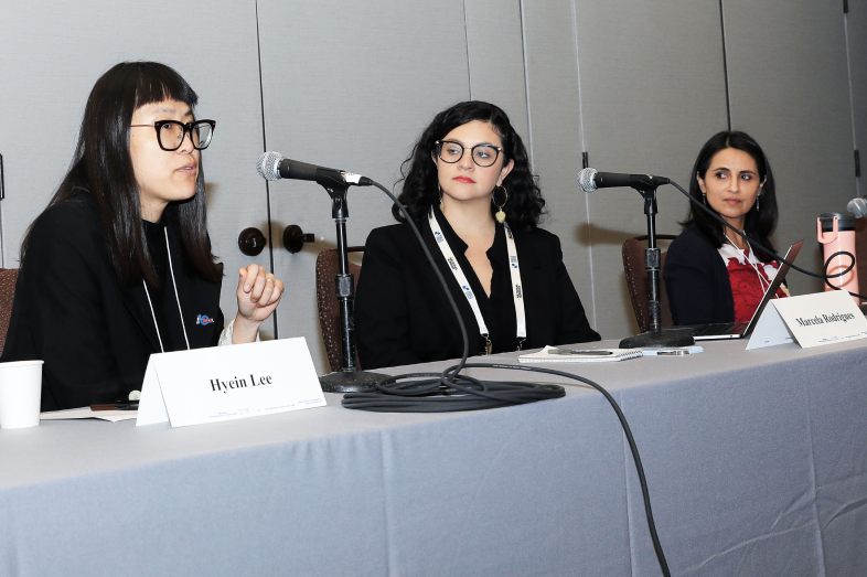 Three women panelists sit at a table with microphones before them.