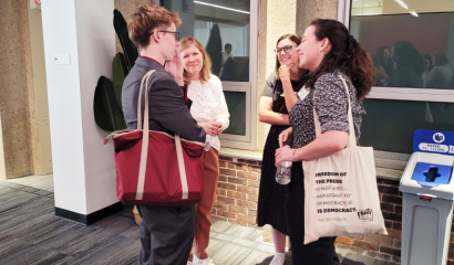 A group of journalists stand together outside a door, talking to each other.