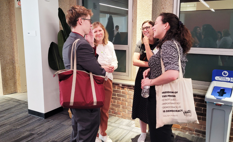 A group of journalists stand together outside a door, talking to each other.