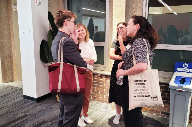 A group of journalists stand together outside a door, talking to each other.