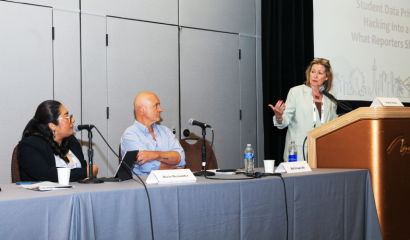 Two people sit at a table while another stands at a podium.