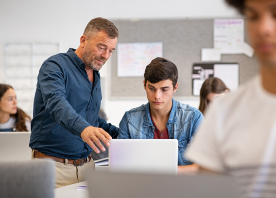 Professor helps student who is on a computer.