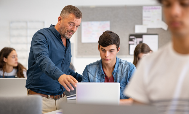 Professor helps student who is on a computer.