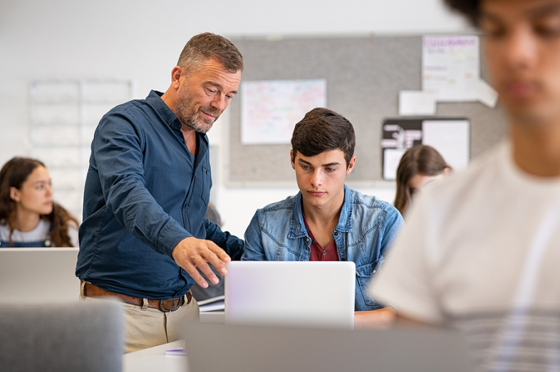 Professor helps student who is on a computer.