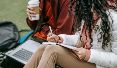 Students sit outside on their computer, drinking coffee.