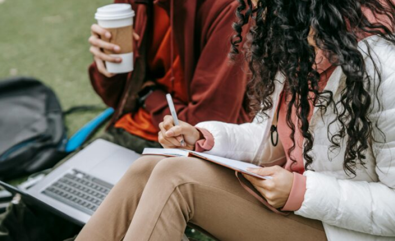 Students sit outside on their computer, drinking coffee.