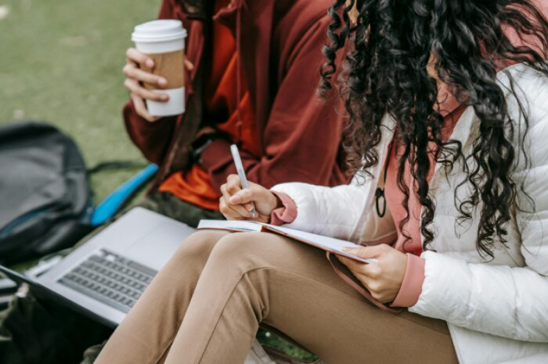 Students sit outside on their computer, drinking coffee.