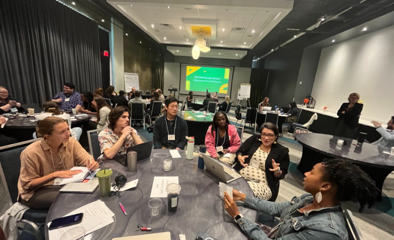 Individuals sit in groups at roundtables, discussing various topics.