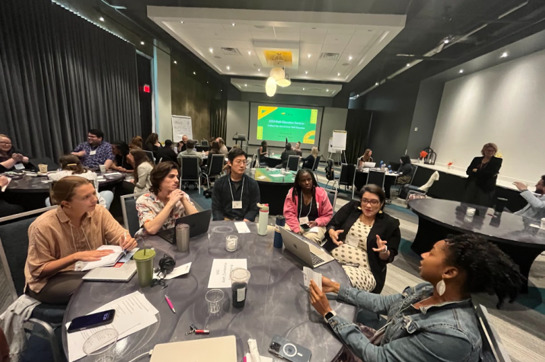 Individuals sit in groups at roundtables, discussing various topics.