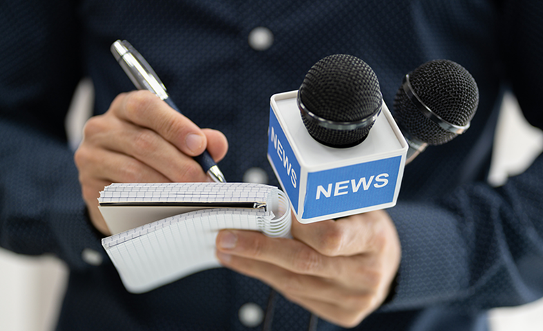 A detailed shot of a reporter scribbling in a notebook and holding a microphone.