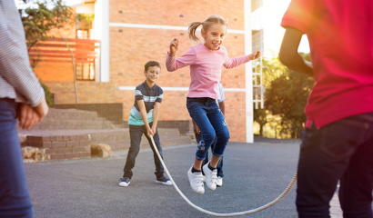 Happy cute girl jumping over skipping rope held by her friends.
