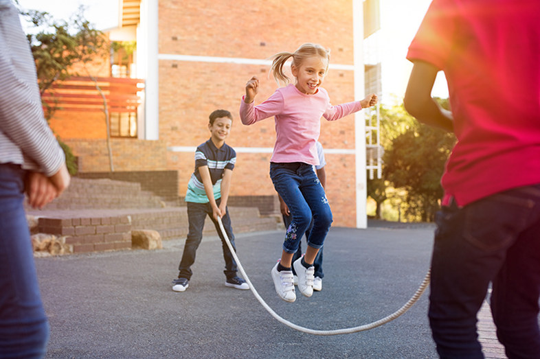 Happy cute girl jumping over skipping rope held by her friends.