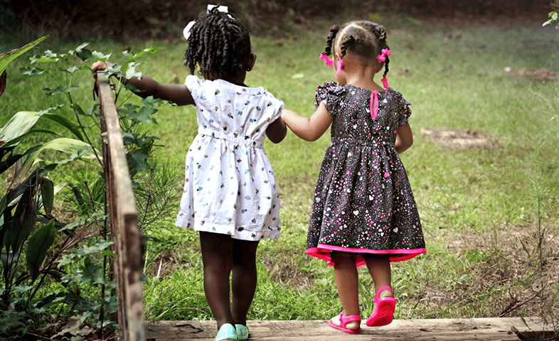 Two little Black girls walk and hold hands.