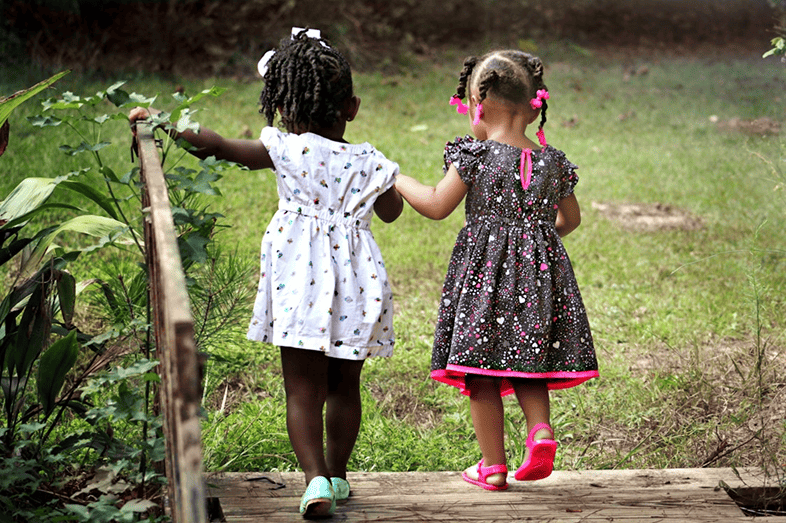 Two little Black girls walk and hold hands.
