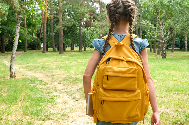 A girl walks through a tree-lined area alone after school.
