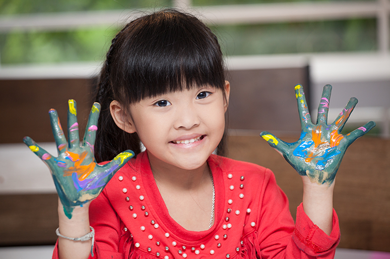 Cute Asian preschooler with paint on her hands.