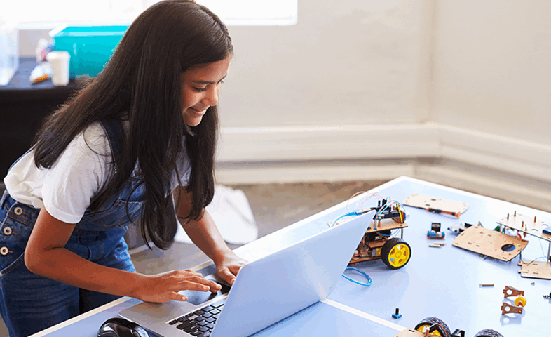 A girl hunches over her computer, near robot parts.