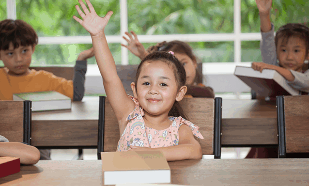 A little girl raises her hand during class at school.