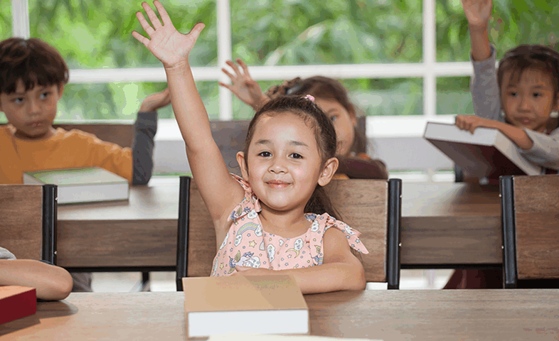 A little girl raises her hand during class at school.