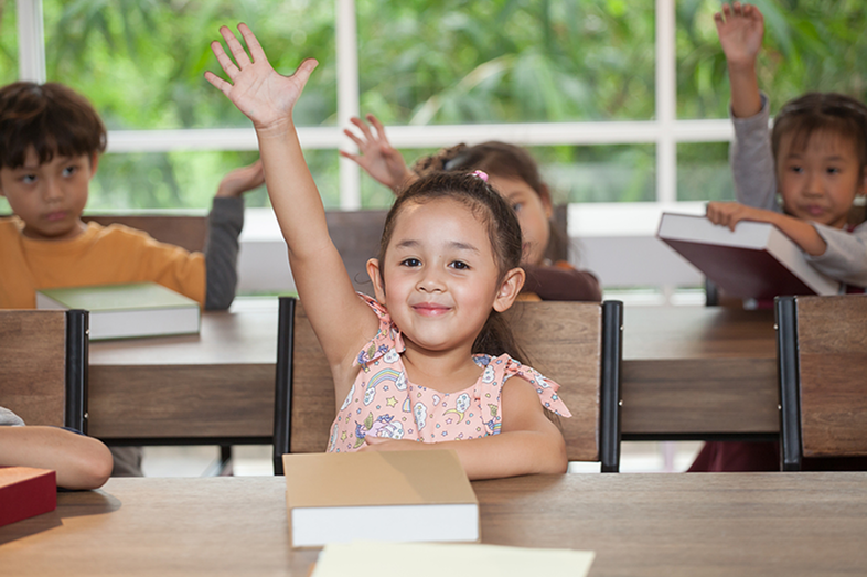 A little girl raises her hand during class at school.