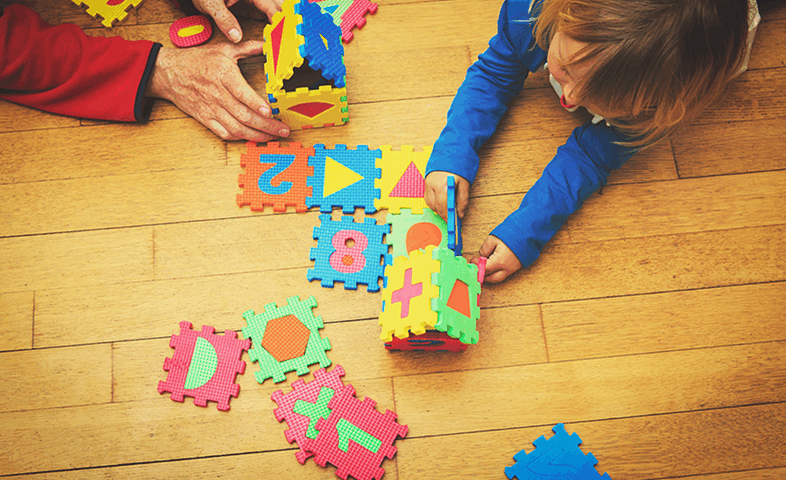 A teacher and child play with a large puzzle.