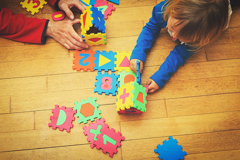 A teacher and child play with a large puzzle.