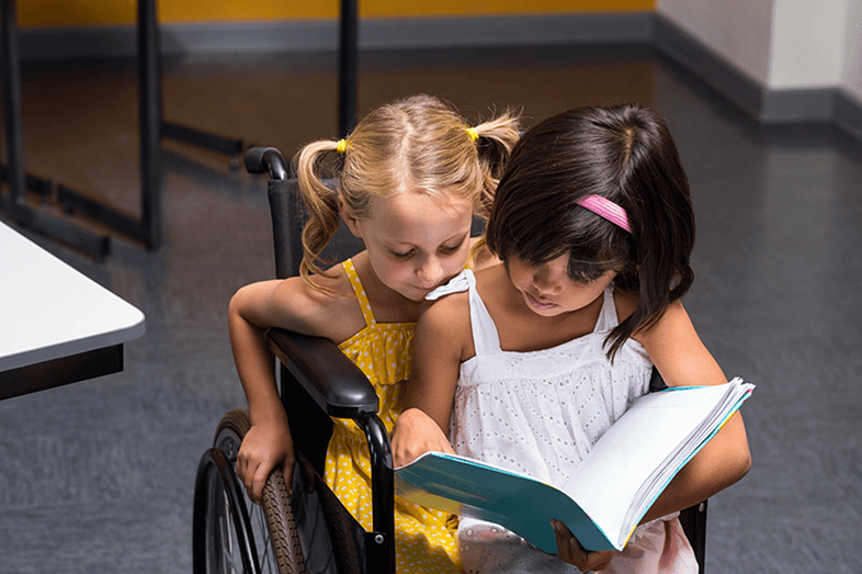 A little girls sits on the lap of a wheelchair bound girl.