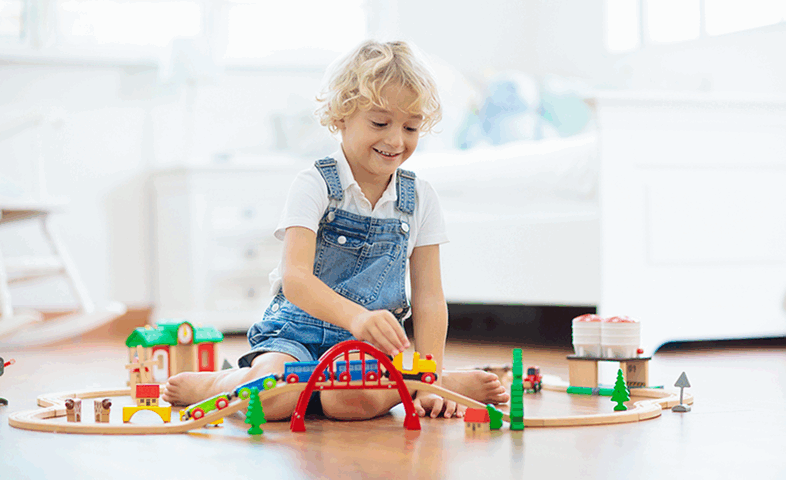A child plays with train tracks on the floor.
