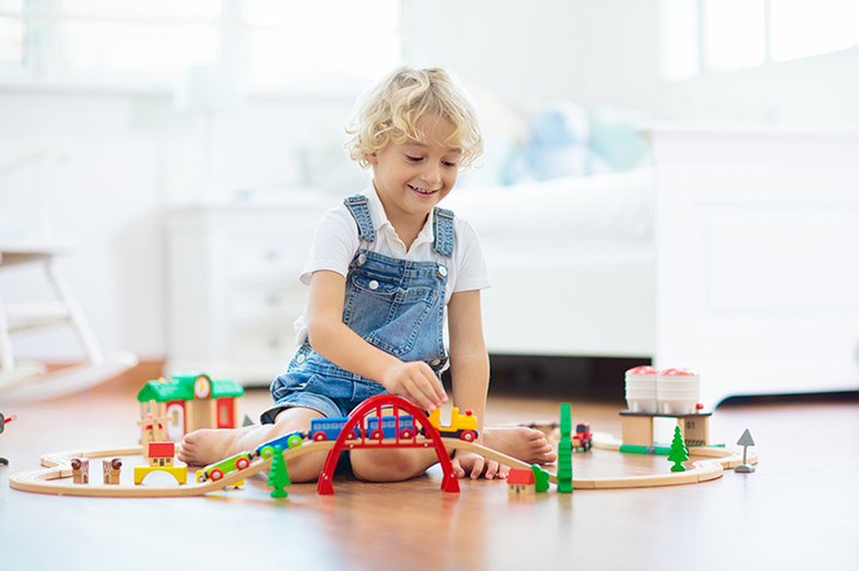 A child plays with train tracks on the floor.
