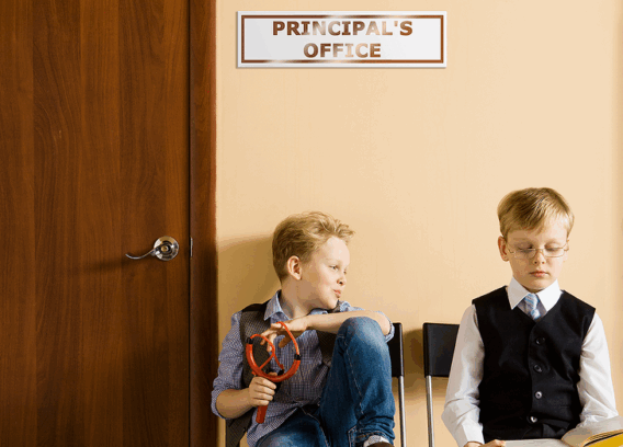 Two schoolboys sitting next to principal's office. They have different behavior and clothes.