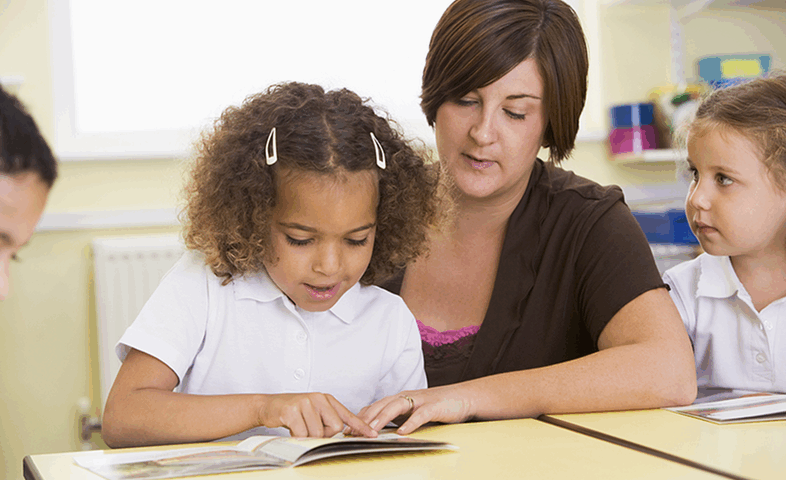 A teacher helps a young girl with reading.