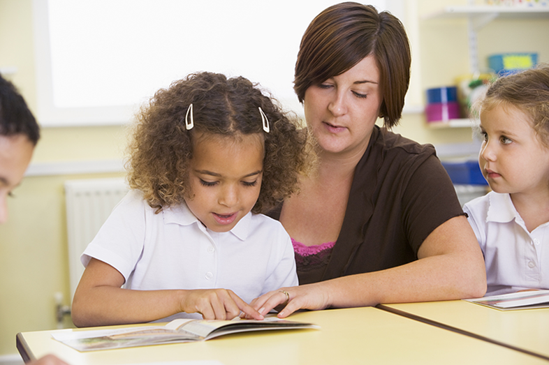 A teacher helps a young girl with reading.